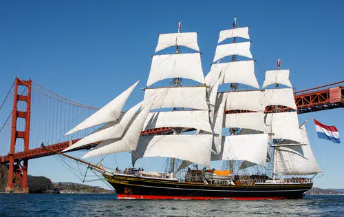 A tall ship under full sail passing the Golden Gate Bridge